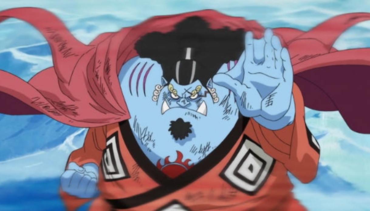 Jinbe, tem cabelos pretos com uns riscos brancos, possui um cavanhaque, tatuagem de um sol no meio do peito e usa um quimono laranja com uma capa vermelha